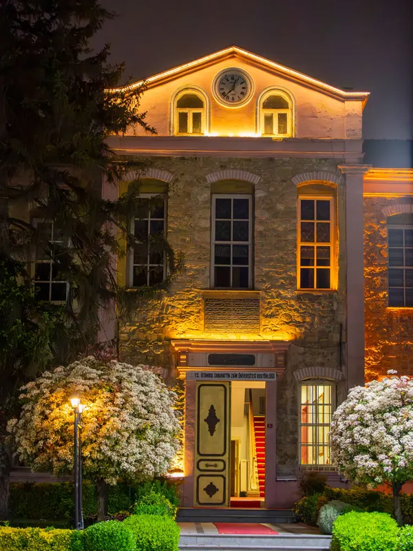 A stone house front lit at night with warm uplights and porch lights