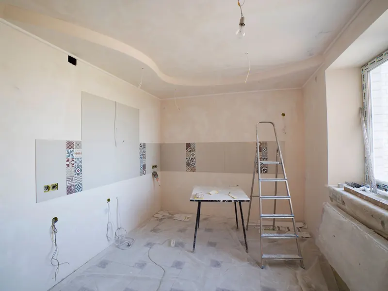 A kitchen stripped to bare walls during a remodel with a stepladder and new wiring stubs
