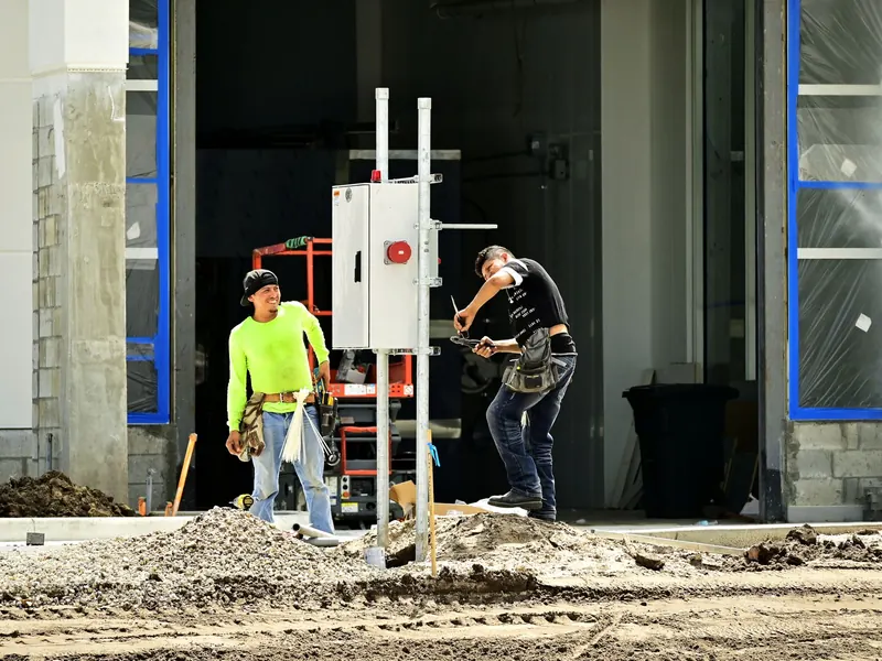 Two electricians setting a power pedestal at a commercial construction site